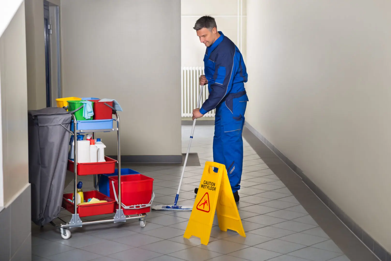 Full length of mature male worker with broom cleaning corridor